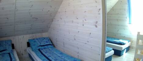 A small, triangular attic bedroom with two beds, each with blue bedding.