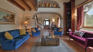 A spacious living room with a high ceiling, a fireplace, and a view through an arched doorway. - VILLA BIDDIZZA an oasis of peace and relaxation (Sicilia)