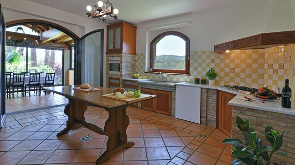 A spacious kitchen with a large island, a dining area with chairs, and a view through an archway.
