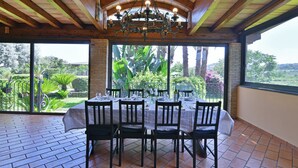A dining area with a table set for six, surrounded by brick walls and large windows offering a view of a lush garden. - VILLA BIDDIZZA an oasis of peace and relaxation (Sicilia)