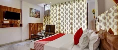 A hotel room with a bed, a television mounted on the wall, a ceiling fan, and patterned curtains.
