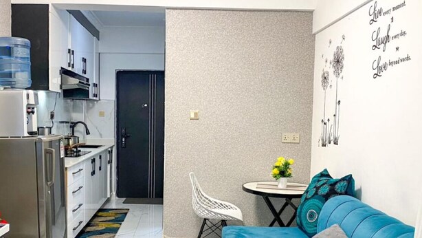Een ruimtelijk ingerichte leefruimte met een kitchenette, een blauwe bank, een eettafeltje en een televisie.