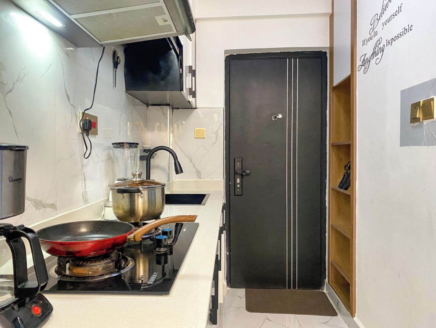 A kitchen with a stove, a pot, and a black refrigerator.