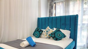 Een bed met een blauwgroen hoofdeinde, witte beddengoed en decoratieve kussens.