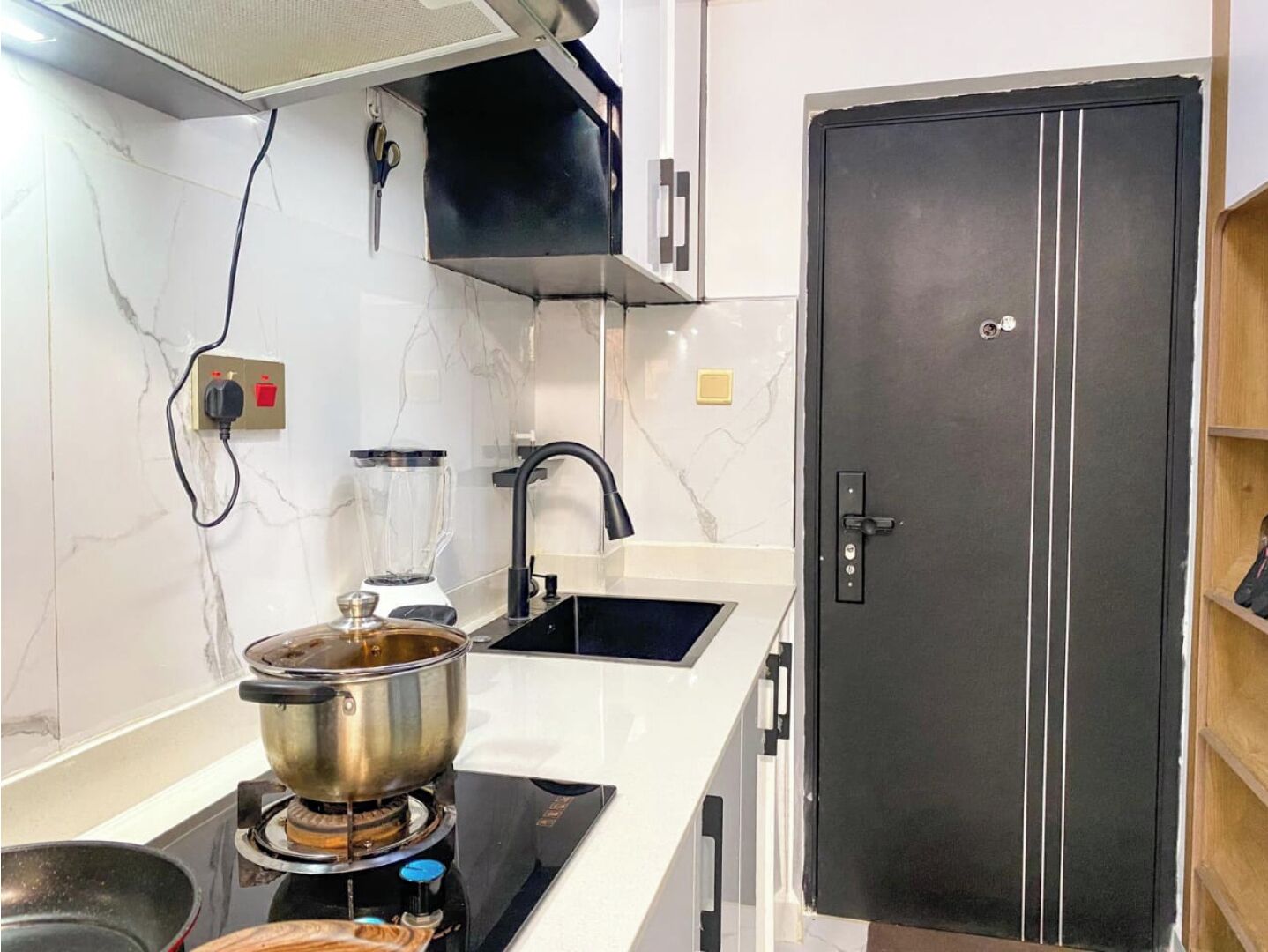 A kitchen with a stove, a sink, a blender, and a black refrigerator.