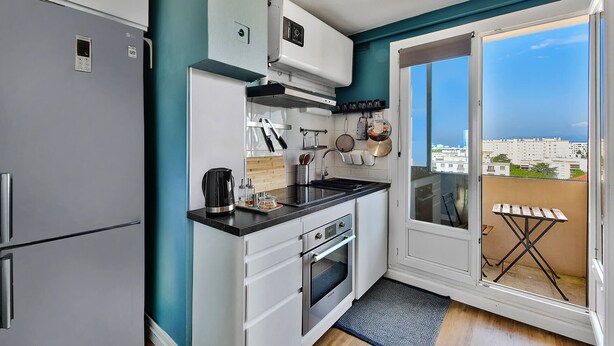 A compact kitchen with a built-in oven, a coffee maker, and a sink. A balcony with a view of the city is visible through a glass door. - T4, Crossing, 3bed, quiet, Metro D'parking 7 /7.  Secure residence. (Vénissieux)