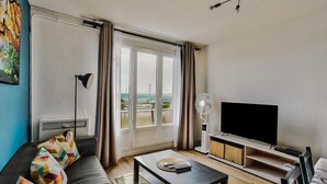 A living room with a sofa, a coffee table, a TV, and a balcony with curtains. - T4, Crossing, 3bed, quiet, Metro D'parking 7 /7.  Secure residence. (Vénissieux)