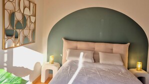 Un dormitorio con cabecera curvada, cama con ropa de cama blanca, dos lámparas de noche y un adorno en la pared.
