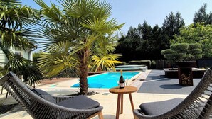 Un área junto a la piscina con sillones de mimbre, una botella de champán y un árbol perfectamente podado al fondo.