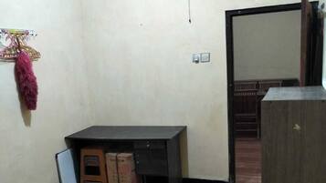 A room with a wooden floor, a desk, a small cabinet, and a fan on the wall.