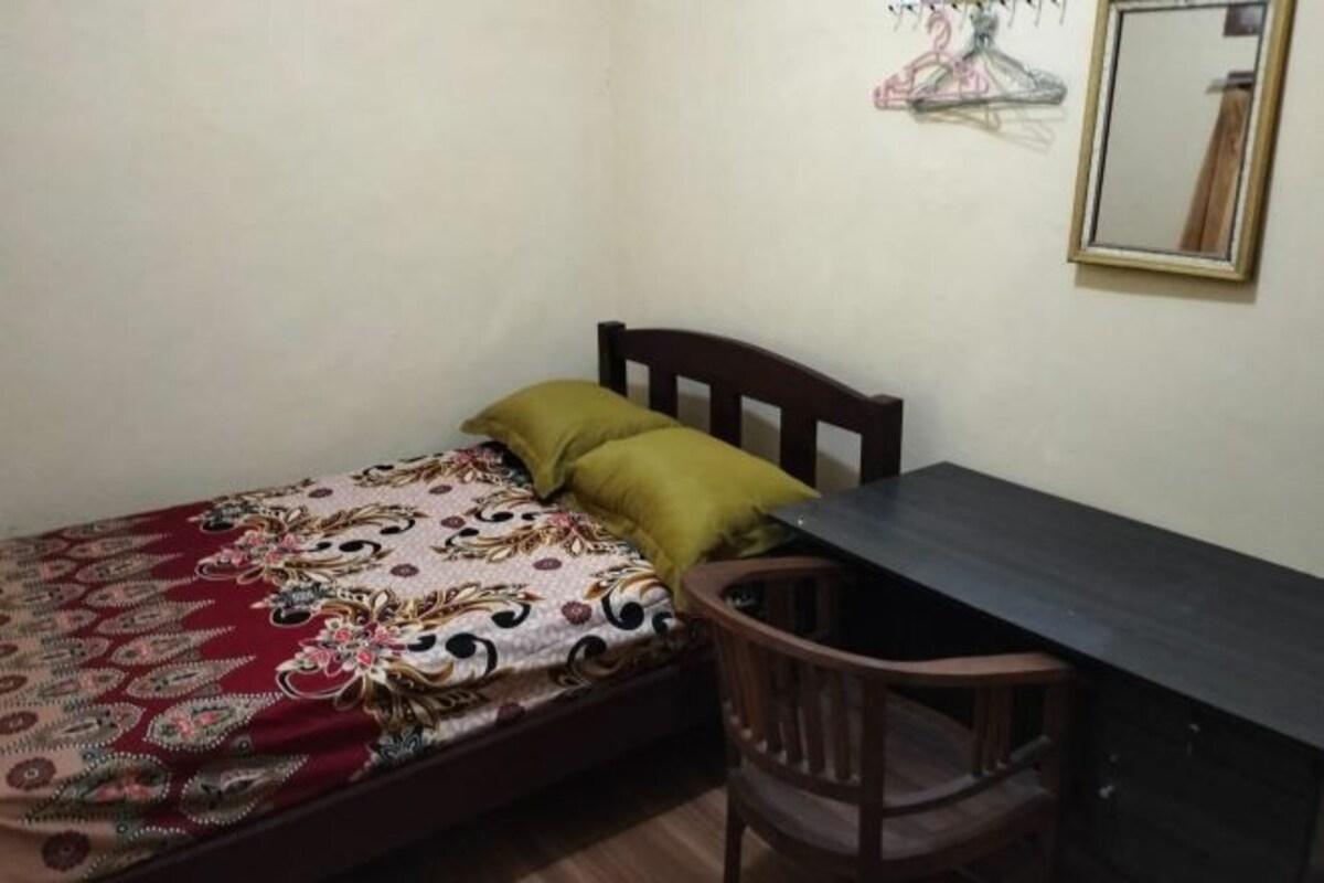Um quarto pequeno com uma cama, uma cadeira de madeira e uma mesa.