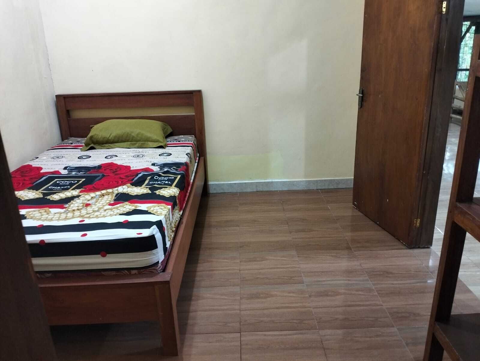 Quarto pequeno e estreito com cama de madeira, travesseiro verde e colcha estampada.