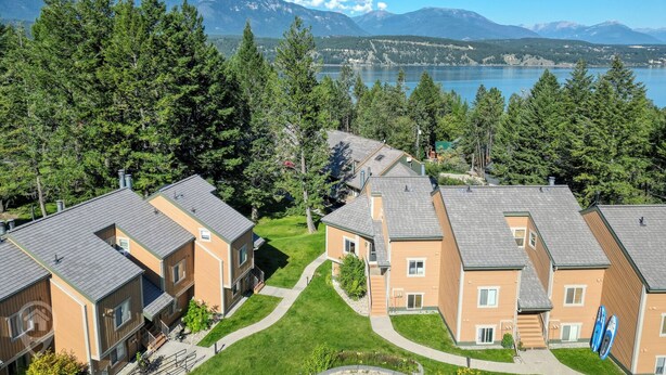 Un quartiere residenziale con case moderne a due piani, un prato curato e un lago con montagne sullo sfondo.