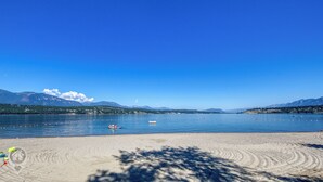 Una spiaggia con cielo sereno, acqua calma e montagne sullo sfondo.