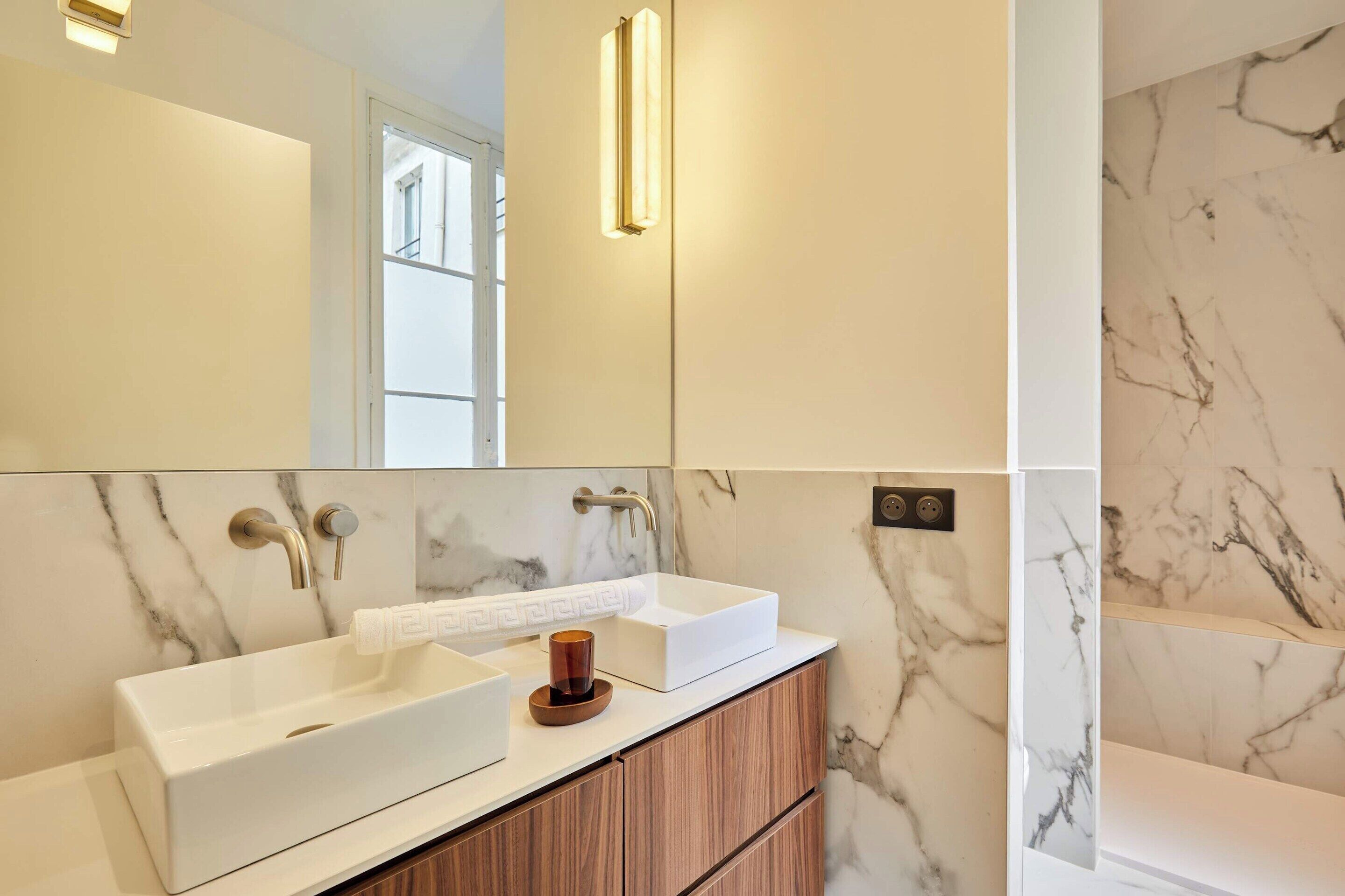 Un baño con dos lavamanos, armarios de madera, paredes de mármol y un espejo.