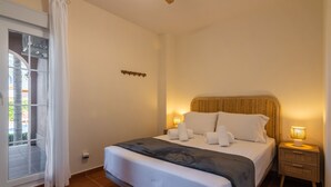 A neatly made bed with white linens and a dark blanket, a bedside lamp, and a window with white curtains. - Los Gavilanes - Isla Canela Beach ICLHG62SP (Isla Canela)