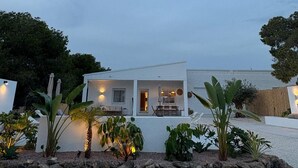 Un edificio moderno blanco con un patio rodeado de plantas tropicales y un muro de piedra.