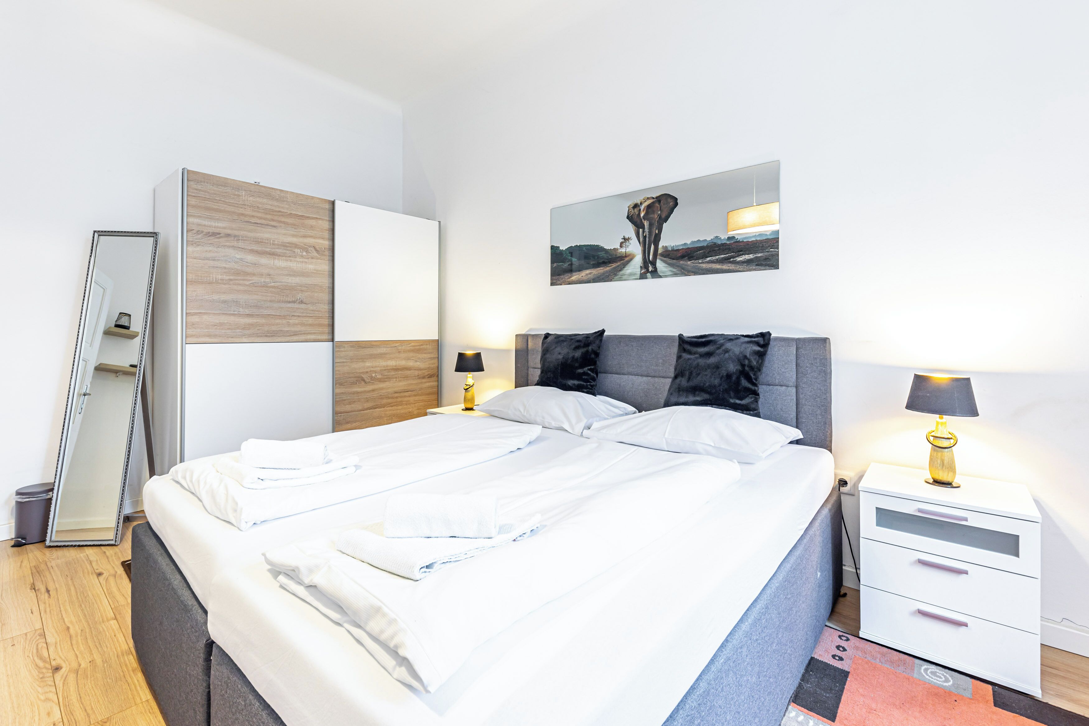 A modern bedroom with a large bed, bedside tables, a mirror, and a wall-mounted picture.