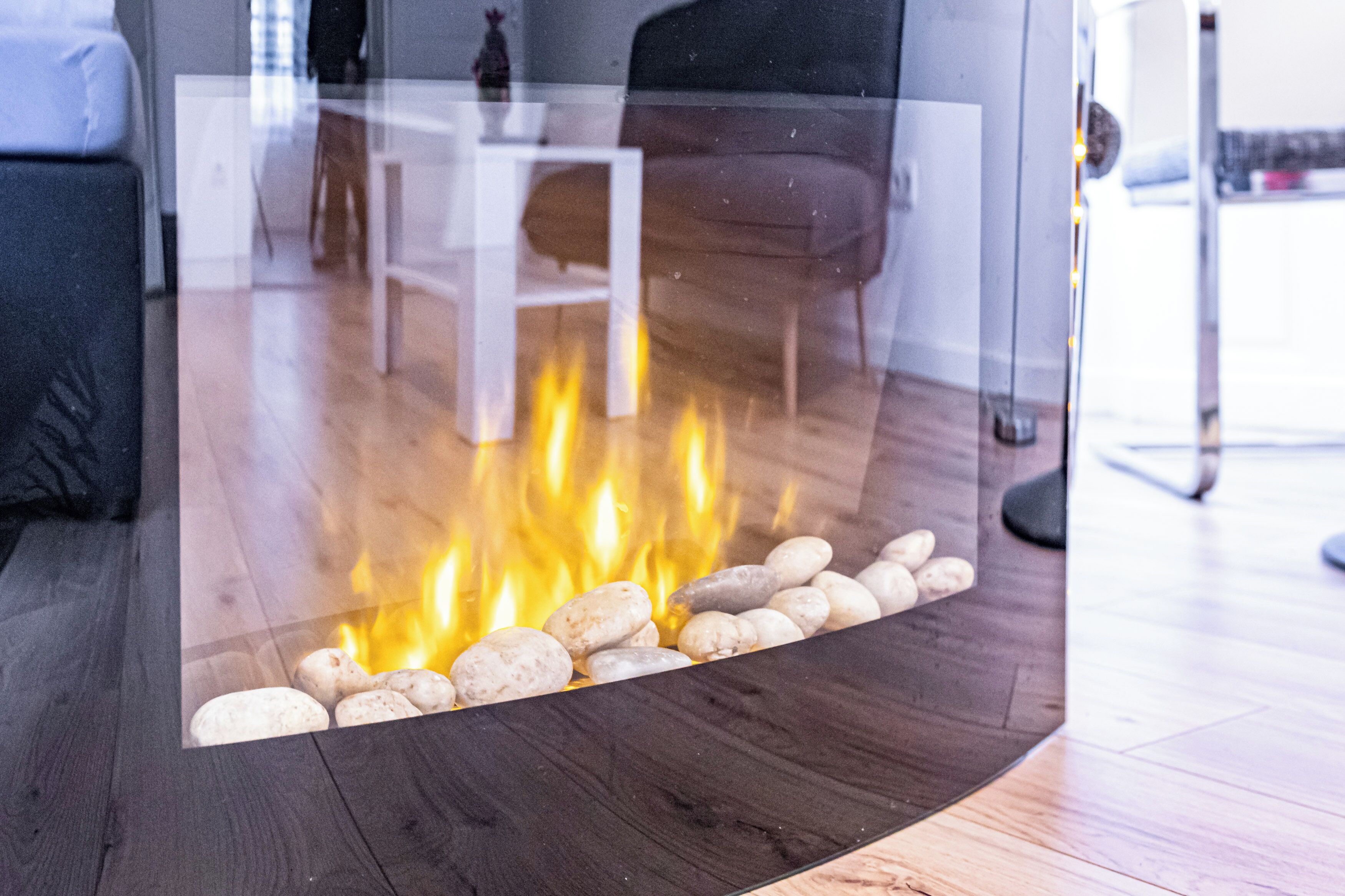Un soggiorno moderno con camino in vetro, pavimento in legno e arredi contemporanei.