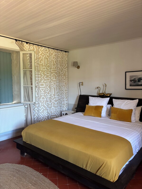 A bedroom with a large bed, a radiator, a window with curtains, and a patterned wall. - Villa Bam Bam (Apt)