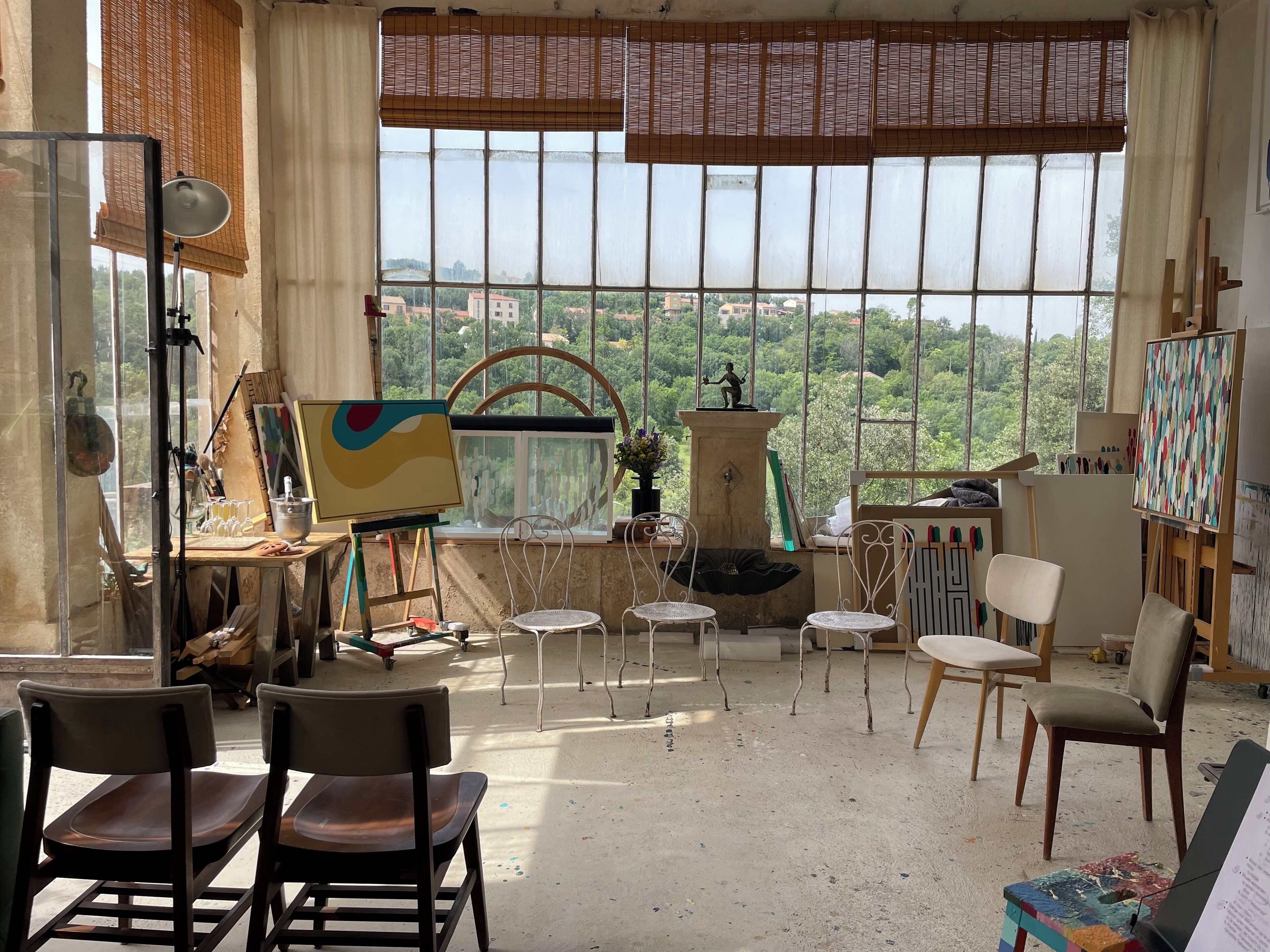 Un estudio de artista con un gran ventanal, caballetes, sillas y material de arte.
