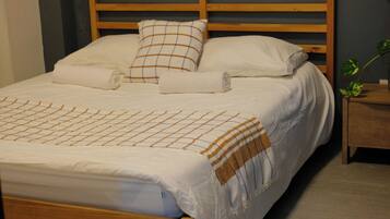 A single bed with a wooden frame, a bedside table with a plant, and a window with blinds.