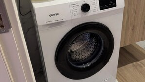 Eine moderne Waschmaschine mit Bedienfeld, einer weißen Spüle obenauf und einer Wand mit Marmorfliesen.