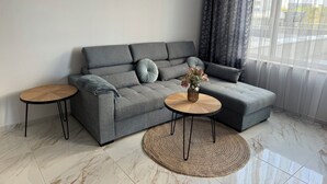 Ein modernes Wohnzimmer mit einem grauen Ecksofa, zwei runden Holztischen, einem gewebten Teppich und einer Blumenvase.
