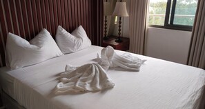 A hotel room with a neatly made bed, pillows, a bedside lamp, and a window with curtains. - Suite Deluxe Beachfront near Mactan Cebu Airport,in Tambuli Seaside Condominiums (Lapu-Lapu)