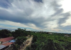 A rural landscape with a dirt road, greenery, and buildings in the distance under a cloudy sky. - Suite Deluxe Beachfront near Mactan Cebu Airport,in Tambuli Seaside Condominiums (Lapu-Lapu)