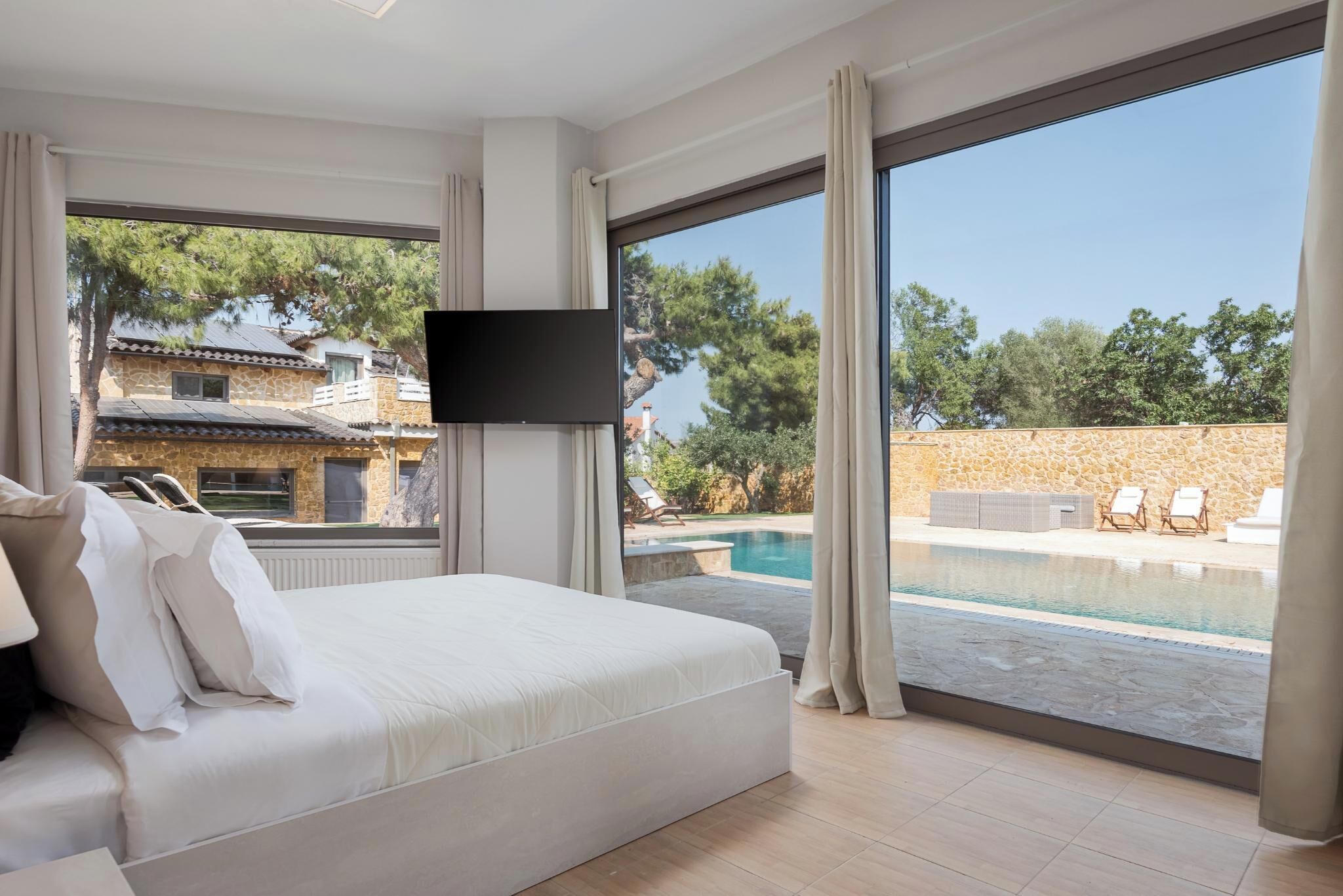 A hotel room with a large bed, a TV mounted on the wall, and a view of a swimming pool through large windows.