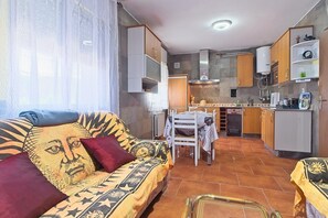 Un salon avec un canapé et une table à manger, une cuisine équipée de meubles et d’appareils électroménagers, et une fenêtre avec des rideaux.