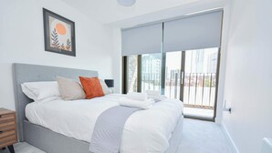 A modern bedroom with a large bed, a nightstand, a framed picture on the wall, and a sliding glass door to the outside. - Central Manchester 2BR Apt in Lomax Street (Manchester)