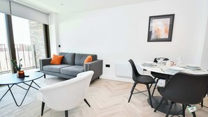A modern living room with a grey sofa, white armchair, and a dining table set for four. - Central Manchester 2BR Apt in Lomax Street (Manchester)