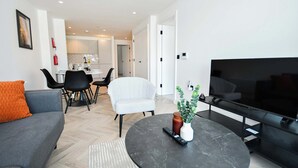A modern living room with a sofa, a dining area, a TV, and a kitchen in the background. - Central Manchester 2BR Apt in Lomax Street (Manchester)