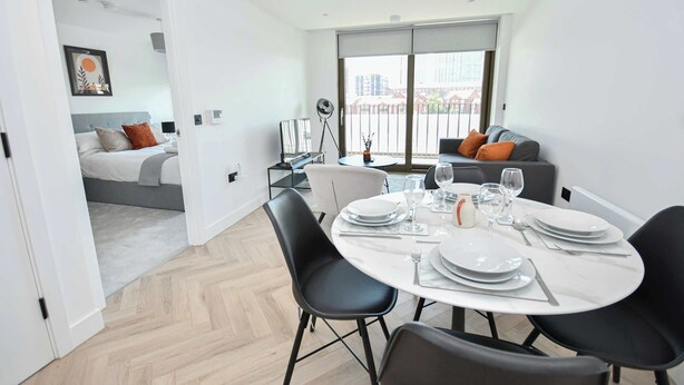 A modern dining area with a round table set for four, a sofa, and a balcony with a view. - Central Manchester 2BR Apt in Lomax Street (Manchester)