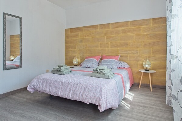 A bedroom with a wooden headboard, a bed with pink and white bedding, two bedside tables with lamps, and a mirror on the wall.
