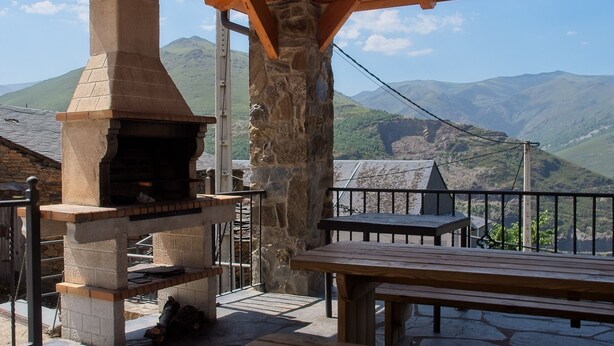 A stone-built outdoor kitchen with a chimney, a wooden bench, and a table.