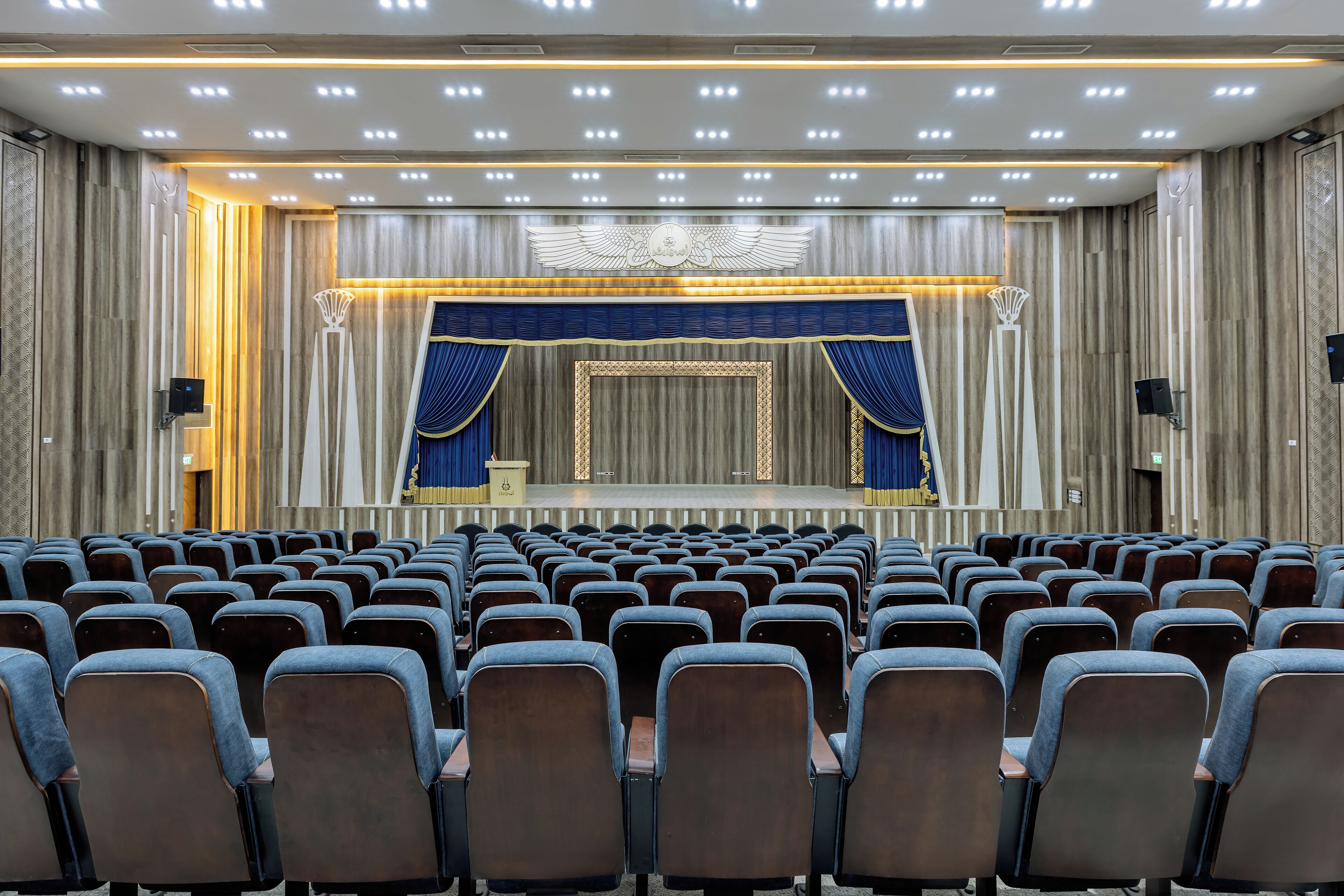 Ein Theater mit Reihen von Sitzen, einer Bühne mit Vorhängen und einer Decke mit Einbaustrahlern.
