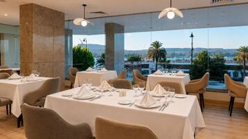 A restaurant with tables set for dining, large windows offering a view of the cityscape, and modern interior design.