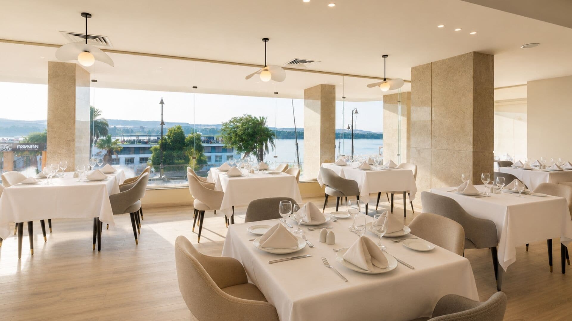 A restaurant with tables set for dining, large windows with a view, and modern lighting fixtures.
