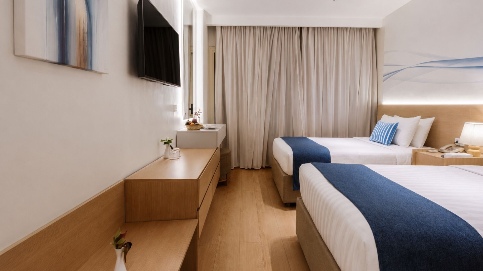A hotel room with two beds, a bedside table, a mirror, a TV, and a window with curtains.
