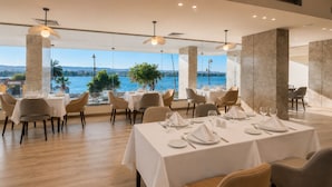 Un restaurante con mesas dispuestas para comer, amplias ventanas con vistas al mar e iluminación moderna.