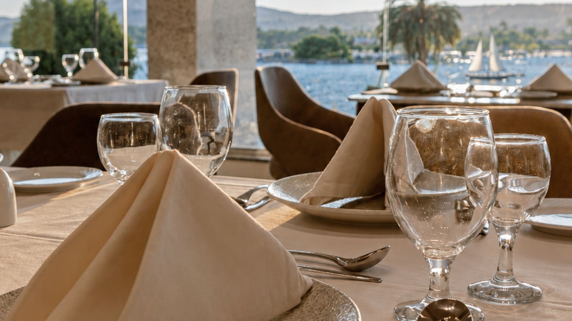 A dining table set with a view of the sea, including boats and a distant shoreline.