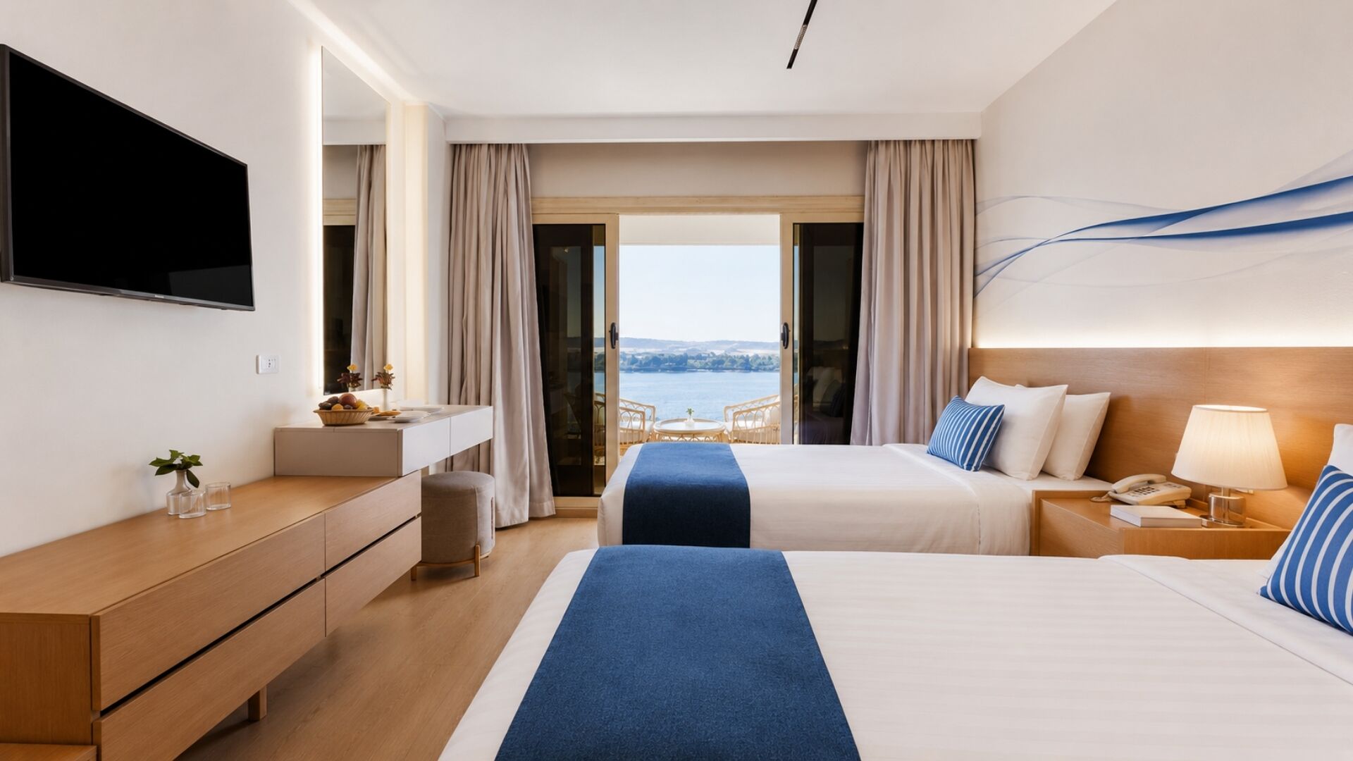 A hotel room with a bed, a desk, a TV, and a view of the sea.