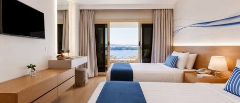 Habitación de hotel con cama, escritorio, televisor y vista al mar.