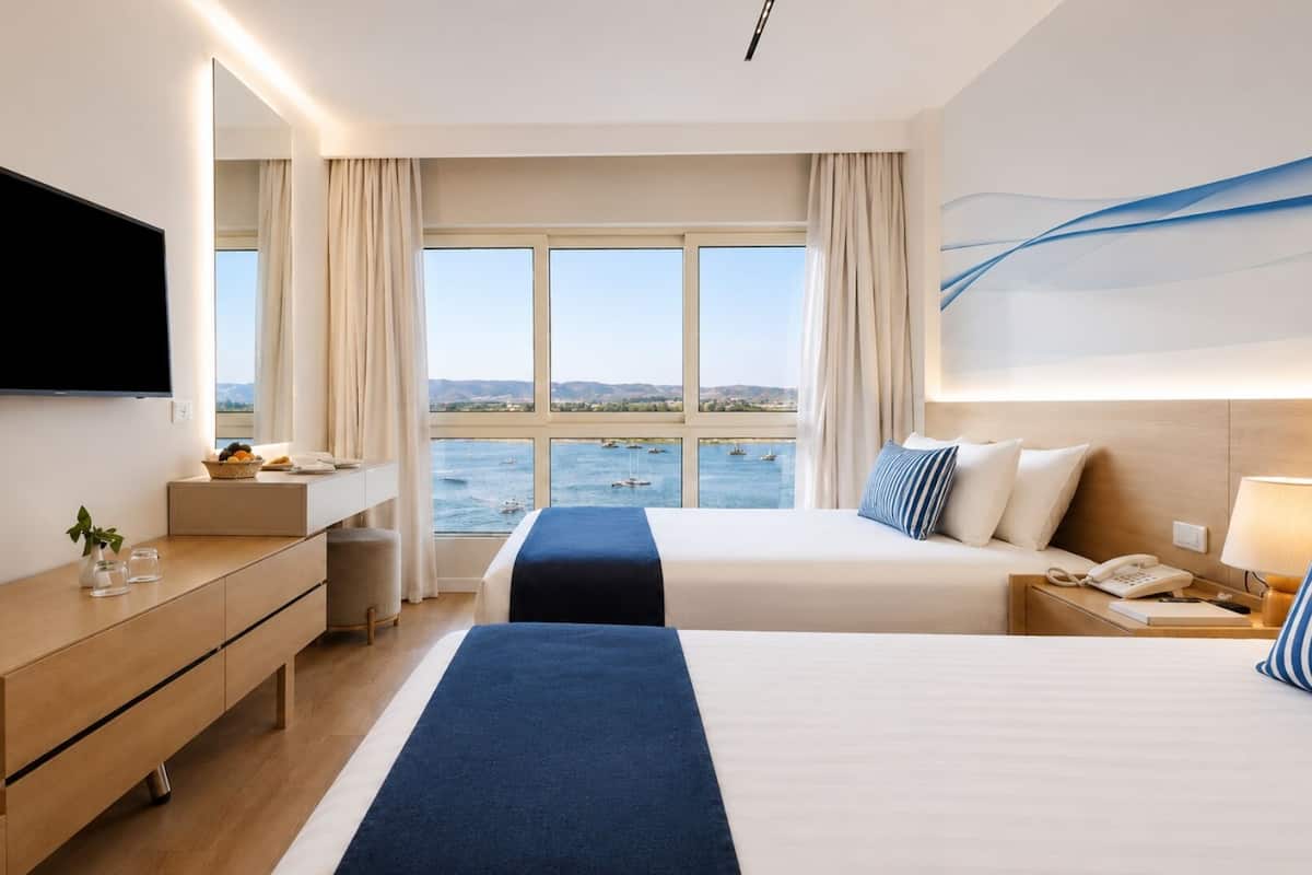A hotel room with a bed, bedside table, TV, and a view of the sea.