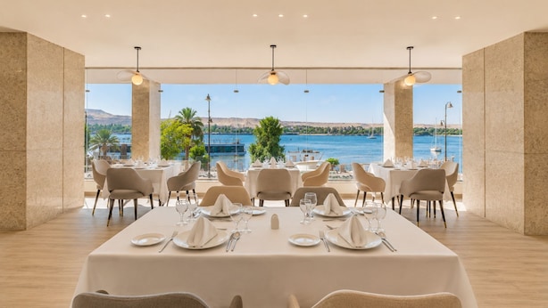 Comedor con mesas dispuestas para cuatro, ventanas amplias con vistas a una masa de agua y colinas distantes.