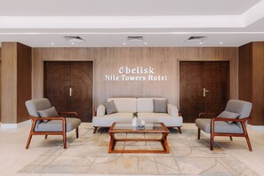A hotel lobby with a sofa, two armchairs, a coffee table, and a wall with the hotel name. - Obelisk Nile Towers (Aswan)