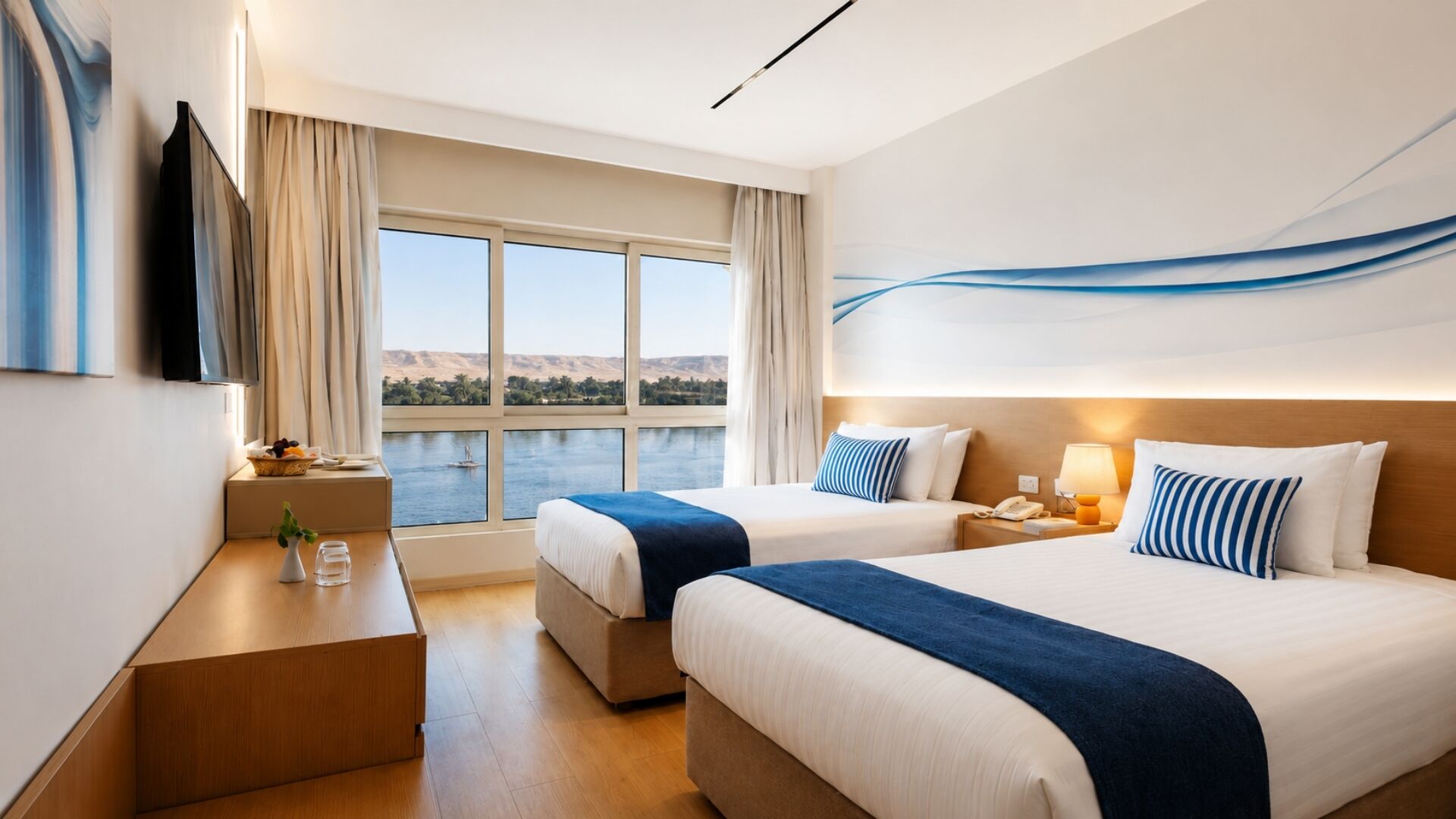 A hotel room with two beds, a desk, a TV, and a large window with a view of a body of water and hills.